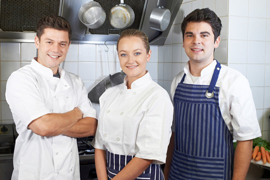 Portrait Of Chef And Staff Standing By Cooker In Kitchen