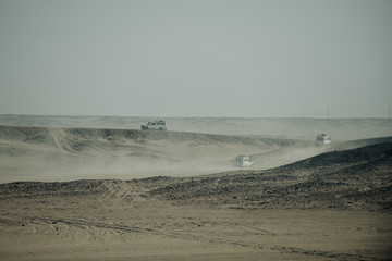 Vehicles racing in desert with sand dust on grey sky