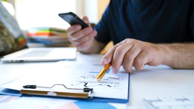 Businessman works with a smartphone and analyzes charts of financial report. Close view and very smooth dolly shot. 4K video with shallow depth of field focus on hands.