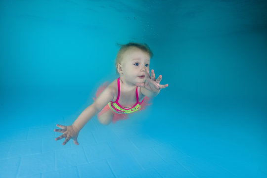 little girl In a yellow swimsuit learns to swim underwater in the pool