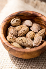 Wooden bowl of salty almond nuts in nutshell