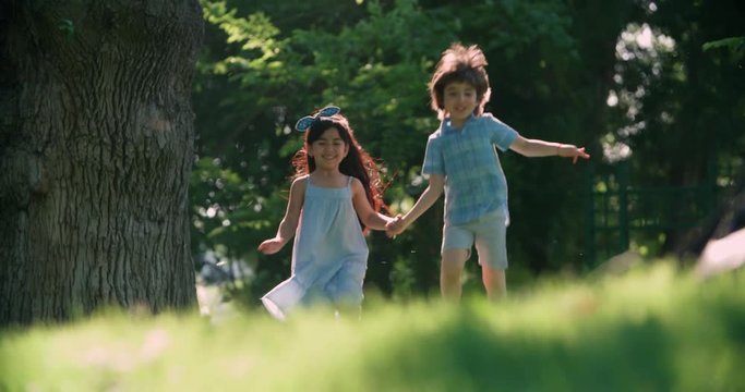 two kids,a boy and a girl running around in the garden holding hands and laughing ,slow motion