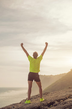 Success of a man after jogging / exercising on a clif near the sea / ocean.