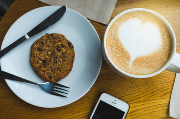 hot coffee heart love with cupcake and smartphone on table  in coffee shop on morning.