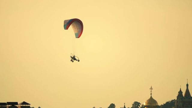 Unknown powered paraglider flying against ancient Russian monastery at sunset