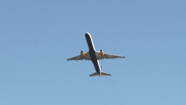 An unidentifiable airplane flying by overhead and traveling through frame leaving a blank clear blue sky.