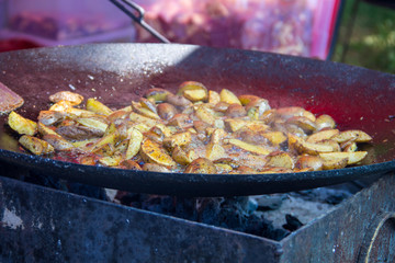 Roasted potatoes cooked outdoors in big metal cauldron pot. Street fast food