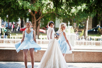 Beautiful bride with bridesmaids posing next to a fountain in the park on a sunny wedding day.