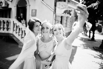 Bride with bridesmaids taking a selfie on city streets. Black and white photo.
