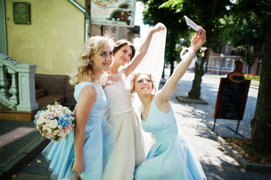 Bride with bridesmaids taking a selfie on city streets.