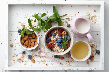 Healthy cereal breakfast with seasonal berries, almonds, farm milk and honey in white wooden tray