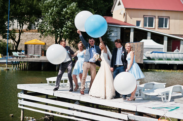 Wedding couple, groomsmen and bridesmaids having fun with balloons on wharf.