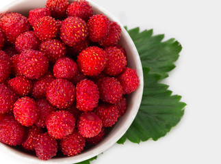 Fresh, ripe wild strawberry in little bowl with green leaves isolated on a white background. Top view, close up.
