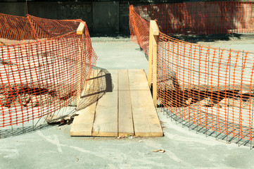 Improvised wooden bridge over the trench on the street construction site for pedestrians and orange...