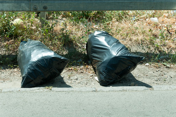 Two plastic black garbage bags thrown on the street. Litter.