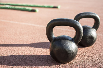 Naklejka na ściany i meble Close up of a kettlebell on a running track. Sport and fitness equipment. Battle rope in the background.