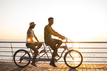 Portrait of a mixed race couple riding on tandem bicycle outdoors near the sea