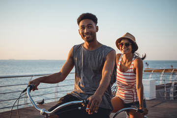 Portrait of a mixed race couple riding on tandem bicycle outdoors near the sea