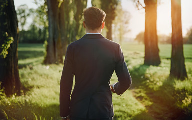 Young businessman walking among majestic, old trees