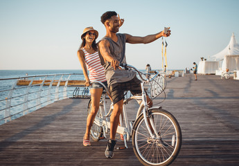 Portrait of a mixed race couple doing selfie on tandem bicycle outdoors near the sea - 164106076