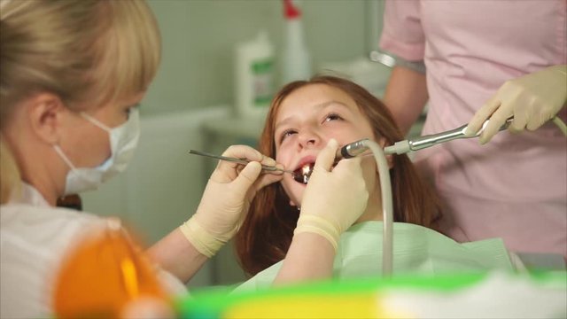 The orthodontist of the dental clinic does the oral cleaning, the young patient is waiting for the completion of the treatment, the nurse is holding the instrument in his hand