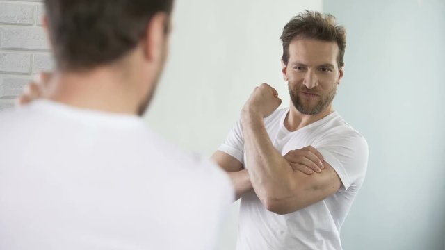 Self-affected macho looking in mirror at his muscles and biceps after workout