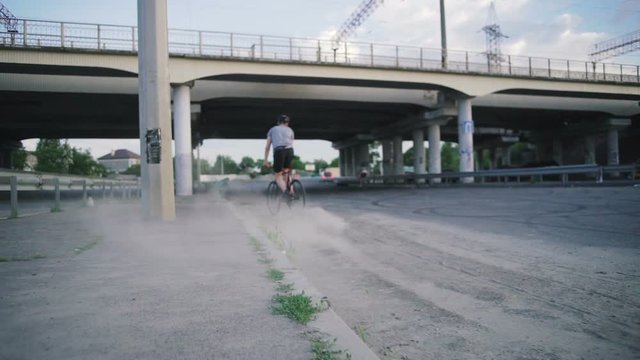 Young hipster man sliding on fixed gear bicycle in dust on the road, slow motion