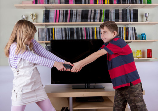 Siblings fighting for the remote control in front of the TV