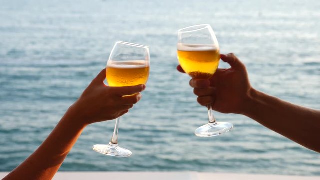 Two people clink glasses with alcohol on the background of the sea. Close-up, slow-motion