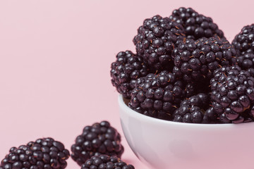 Closeup of a white bowl of fresh red raspberries on a pink background. Copy space
