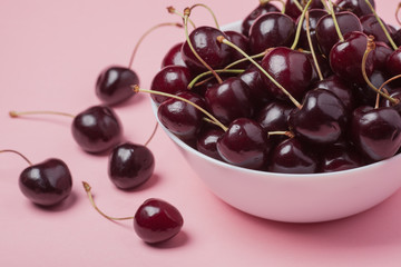 White bowl of fresh red cherries on a pink background. close-up