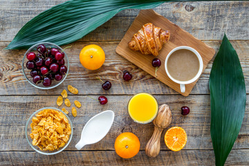 Light tasty breakfast. Muesli, oranges, cherry, french croissant and milky coffee on wooden table background top view