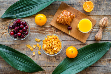 Preparing healthy summer breakfast. Muesli, oranges, cherry, juice on wooden table background top view