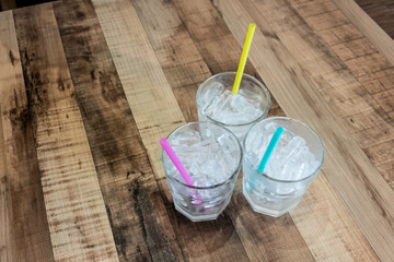 Three glass of tube ice with different color straws on wooden table from high angle. Family dining serve. Selective focus.