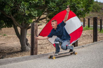 Parachute downhill skateboarder has sail full of wind as he rides goofy foot on his board. 