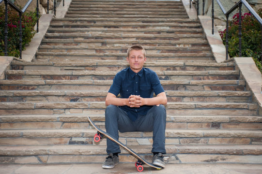 California skateboarder seated on slate stairs holding board with foot.