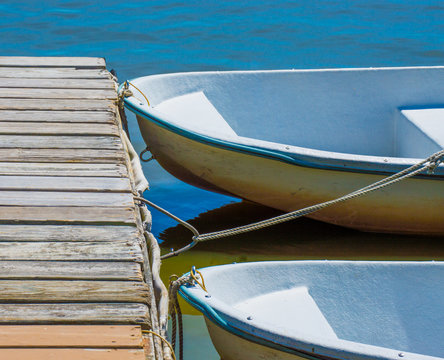 2 small rowboats tied to a weathered wooden dock on a Massachusetts lake