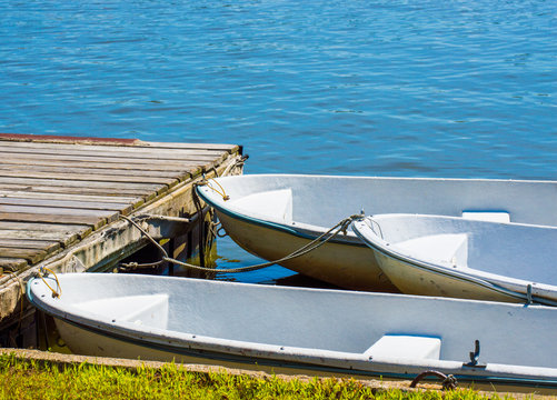 3 small rowboats tied to a weathered wooden dock on a Massachusetts lake