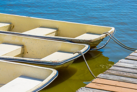 3 small rowboats tied to a weathered wooden dock on a Massachusetts lake