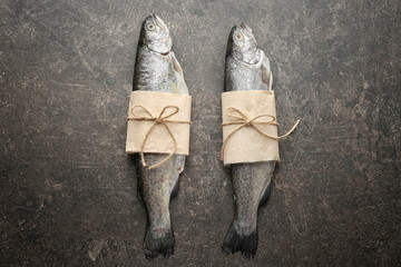 Fresh trout fish wrapped in paper on gray background