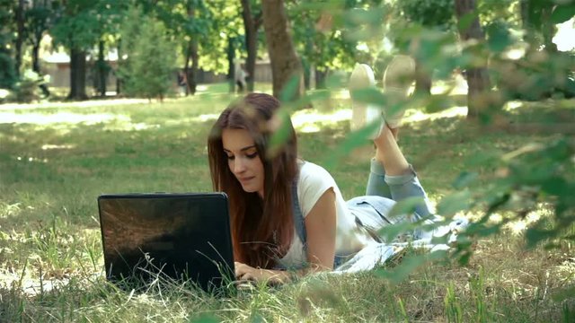 charming lady looks in laptop lying on the green grass