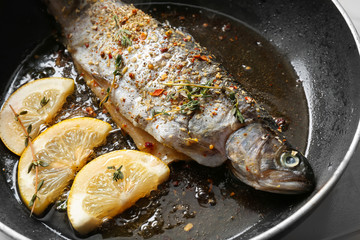 Frying pan with tasty trout fish and lemon slices, closeup