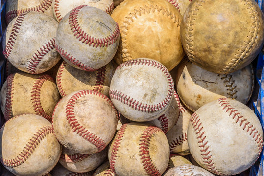 box of old baseballs and softballs in sunlight