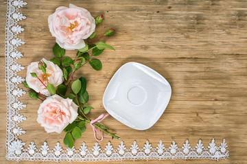flat lay of pink roses with empty white sauser on a wooden table with lace frame and copy space for your text
