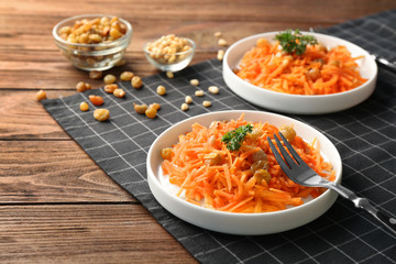 White plates with yummy carrot raisin salad with pine nuts on black checkered napkin
