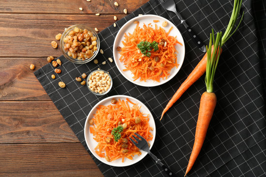 White plates with yummy carrot raisin salad with pine nuts on black checkered napkin, top view