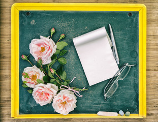 Back to school congrats concept, Roses, pen, glasses and textbook laying on the small chalkboard, Top view with copy space on the empty textbook.