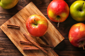 Apples with cinnamon sticks and cutting board on wooden background