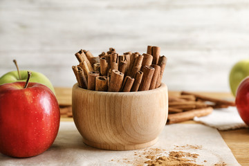 Bowl with cinnamon sticks and apples on table