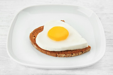 Plate with delicious sunny side up egg and bread slice on wooden background